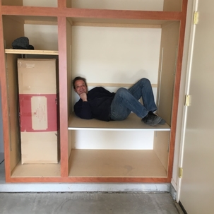 A man is relaxing inside a light-colored garage cabinet.